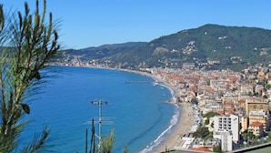 Eine Küstenstadt mit Strand, Gebäuden und einer Hügelkette im Hintergrund.