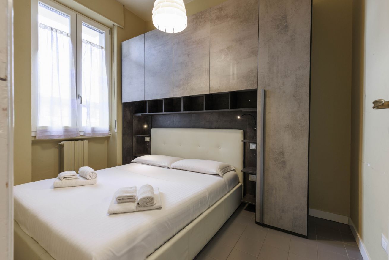 Een moderne slaapkamer met een groot bed, ingebouwde kasten en een raam met dunne gordijnen.
