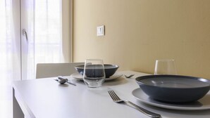 Mesa de jantar posta com uma tigela escura, um copo, um garfo e uma faca.