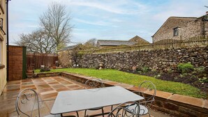 A patio with a table and chairs, a stone wall, and a grassy area with a tree. - Host and Stay 36 Hardy Meadows (Skipton)