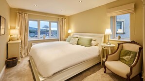 A spacious bedroom with a large bed, two bedside tables with lamps, a chair, and a window with curtains. - Host and Stay 36 Hardy Meadows (Skipton)
