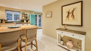 A modern kitchen with a wooden island, bar stools, a white console table, and a framed artwork on the wall. - Host and Stay 36 Hardy Meadows (Skipton)