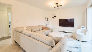 A modern living room with a sectional sofa, a round coffee table, a flat-screen TV, and a white armchair. - Host and Stay The Cosy Corner (Canterbury)
