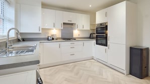 A modern kitchen with white cabinets, a stainless steel sink, a gas stove, and a built-in oven. - Host and Stay The Cosy Corner (Canterbury)