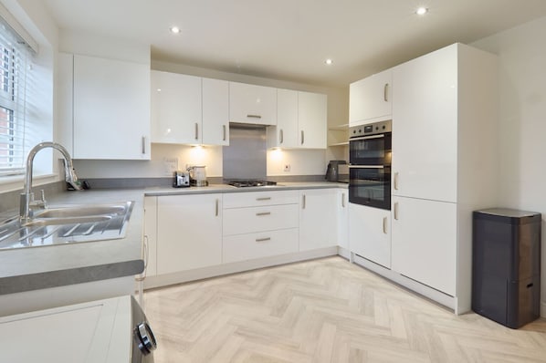 A modern kitchen with white cabinets, a stainless steel sink, a gas stove, and a built-in oven. - Host and Stay The Cosy Corner (Canterbury)