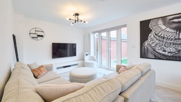 A modern living room with a large sofa, a flat-screen TV, and a large window. - Host and Stay The Cosy Corner (Canterbury)