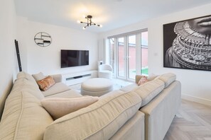 A modern living room with a large sofa, a flat-screen TV, and a large window. - Host and Stay The Cosy Corner (Canterbury)