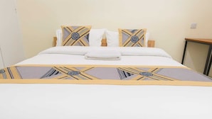 Een net opgemaakt bed met een gebedrukte sprei, witte kussens en een opgevouwen handdoek.