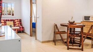 A compact living space with a kitchenette, a dining area with a wooden table and chairs, a sofa with plaid cushions, and a window with a view of the desert. - Apartment  by Interhome (St Antoni de Calonge)