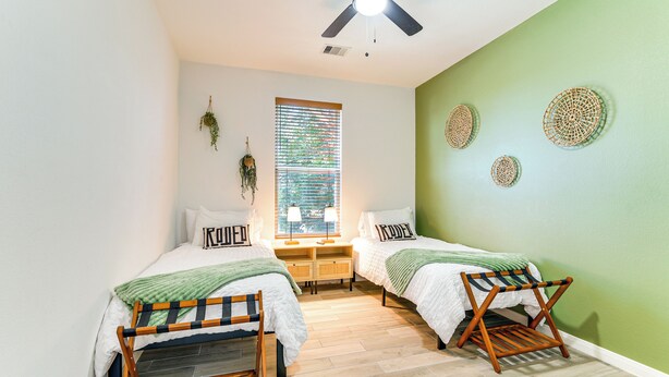 Ein Schlafzimmer mit zwei Betten, einem Deckenventilator, einem Fenster mit Jalousien und einer grünen Wand mit Dekoration.