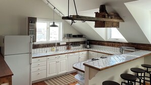 Una cocina con vigas de madera, un refrigerador blanco, una isla grande con taburetes y una lámpara colgante.