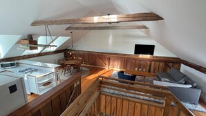 Un dormitorio estilo loft con techo inclinado, una viga de madera en el techo, una cama, un televisor y una kitchenette con microondas y estufa.