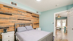 Un dormitorio con cabecera de madera, cama con colcha gris, mesita de noche y cómoda blanca.