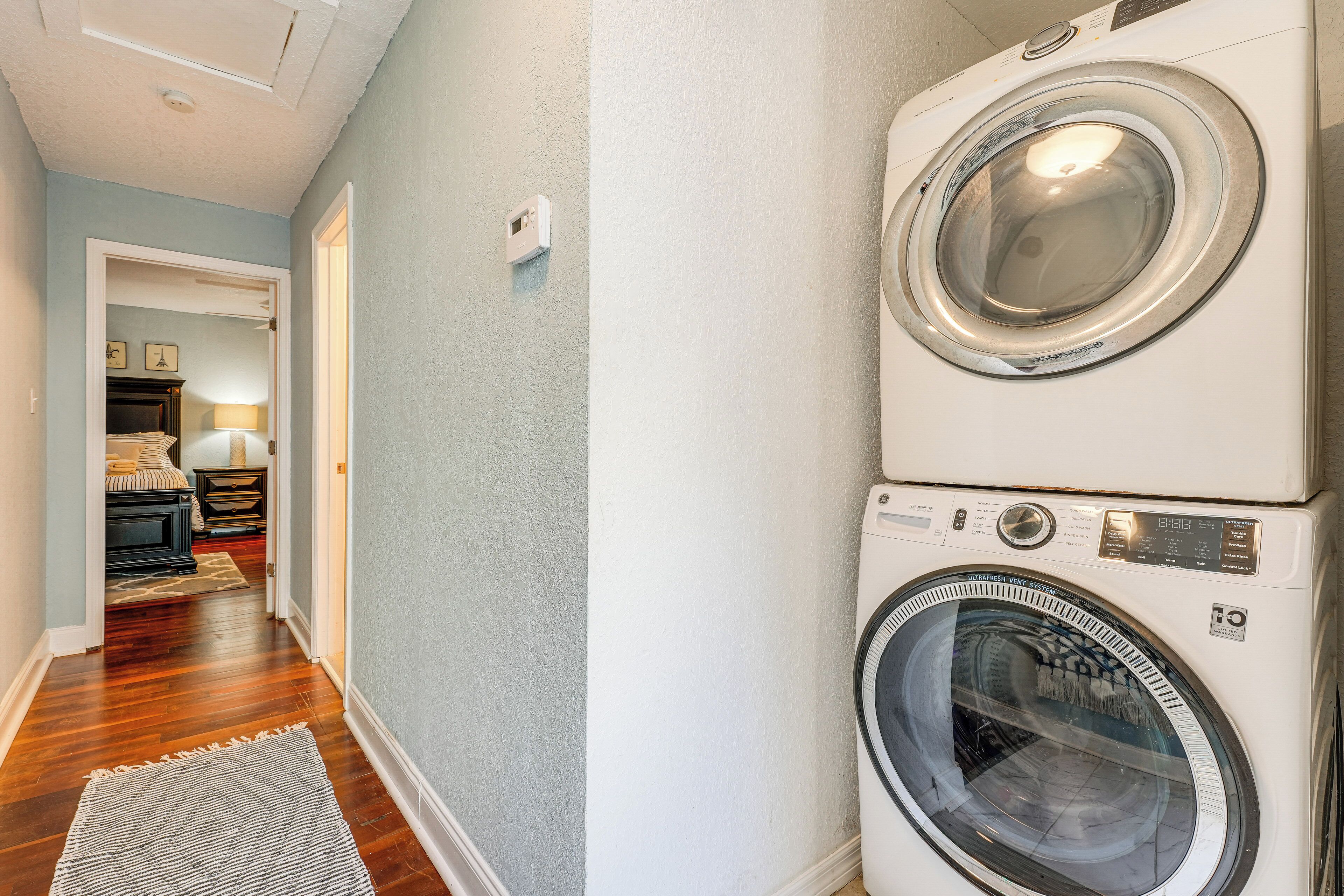 A laundry room with stacked front-loading washers and dryers, a wooden floor, and a hallway leading to a bedroom area.