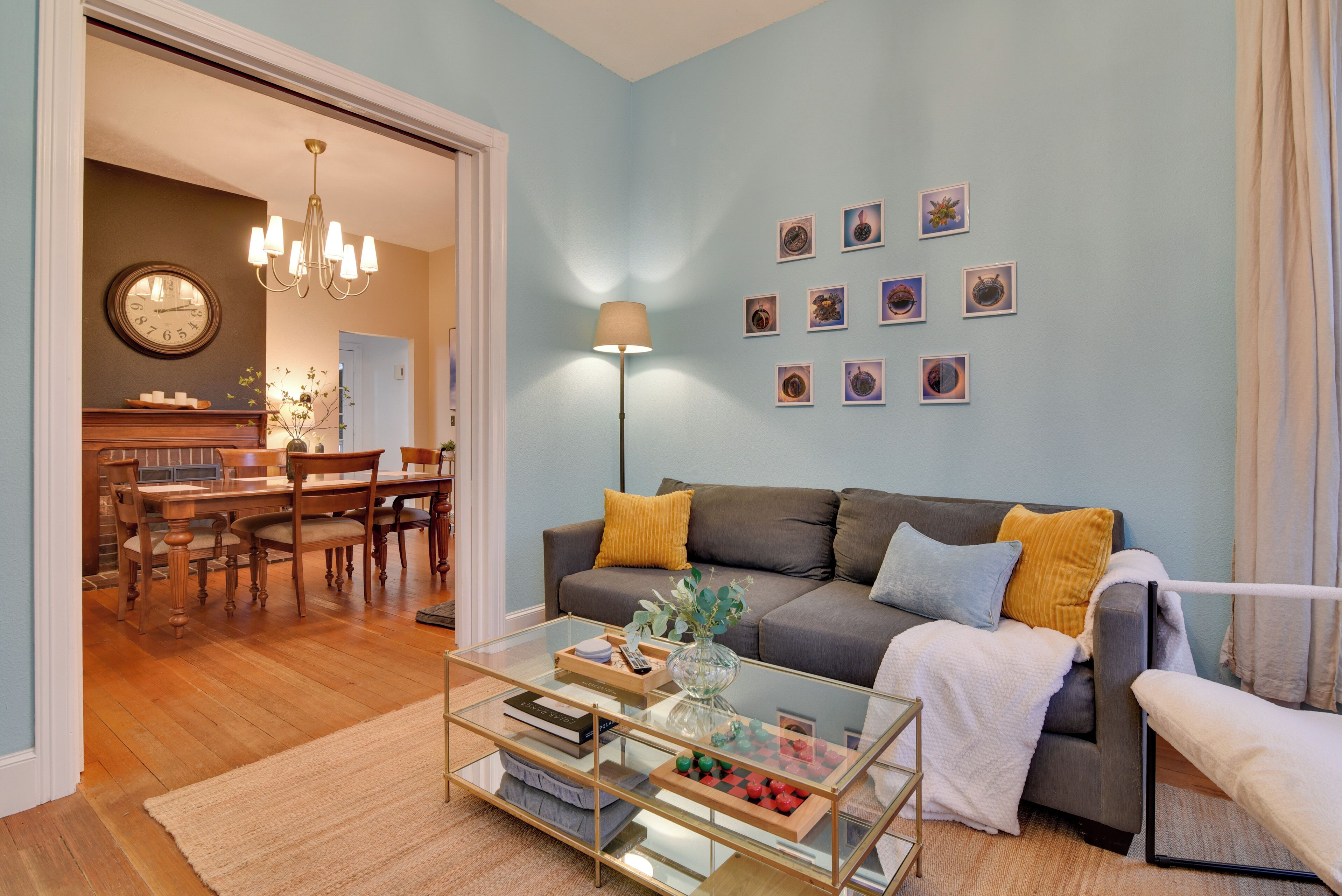 A living room with a sofa, coffee table, and wall art. There is a dining area with a table and chairs visible in the background.