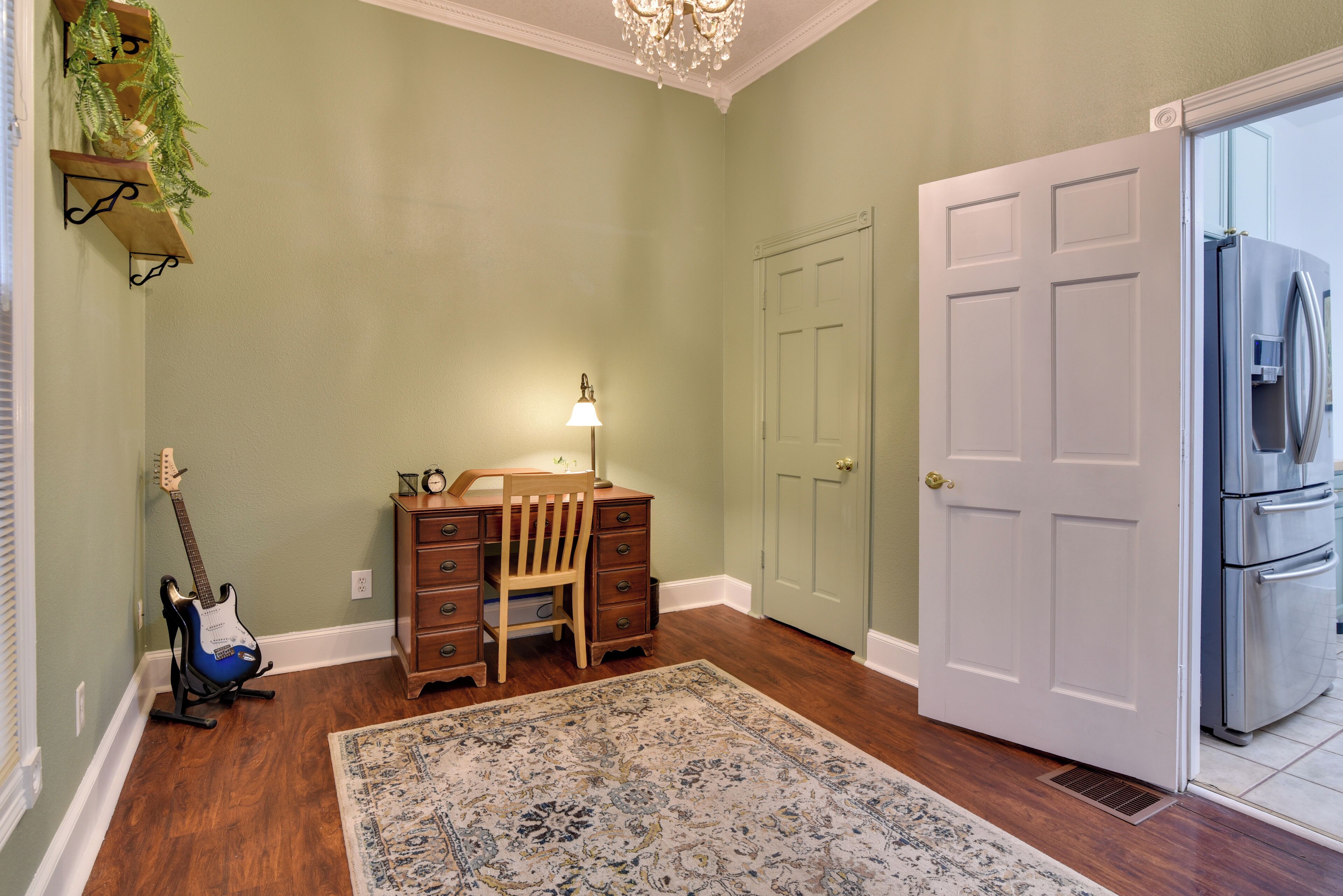 A room with a desk, chair, guitar, lamp, and a refrigerator.