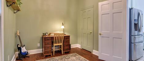 A room with a desk, chair, guitar, lamp, and a refrigerator.