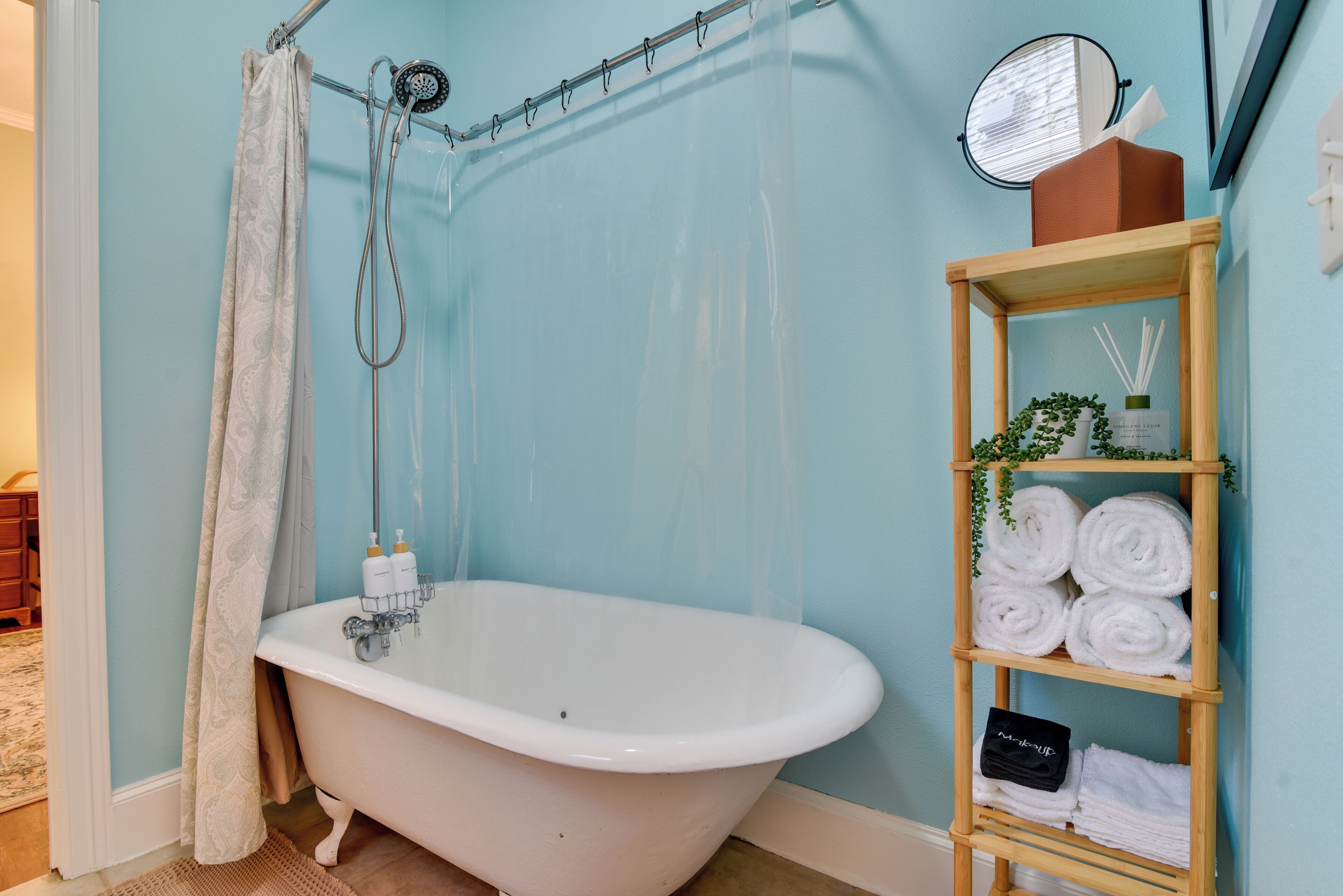 Un bagno con una vasca freestanding, uno scaffale in legno con asciugamani e una tenda da doccia.