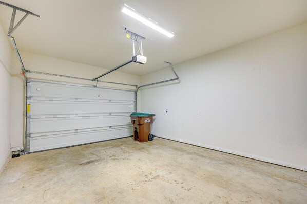 A clean, empty garage with a closed garage door, a ceiling-mounted projector, and a trash bin. - Shop, Dine & Explore: San Antonio Family Retreat! (San Antonio)
