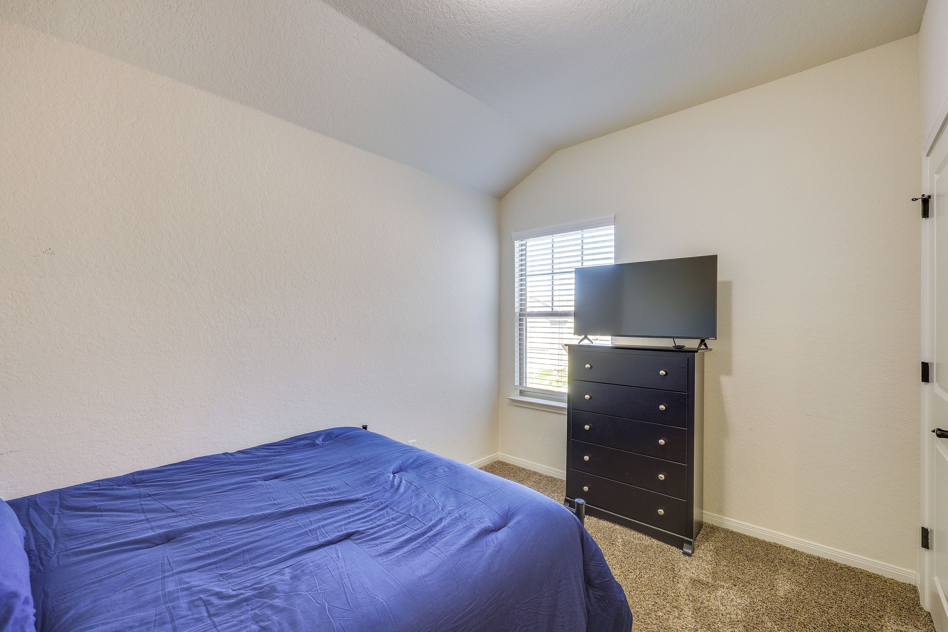 A bedroom with a bed, a dresser, a television, and a window.