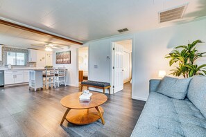 Un vaste espace de vie comprenant un salon avec une table basse ronde en bois, un canapé gris et un coin repas avec un banc et des chaises.