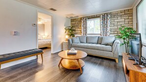 A modern living room with a grey sofa, a round wooden coffee table, a bench, and a television on a wooden stand. - Florida Adventure Hub Near Top Attractions & Lakes (St. Cloud)