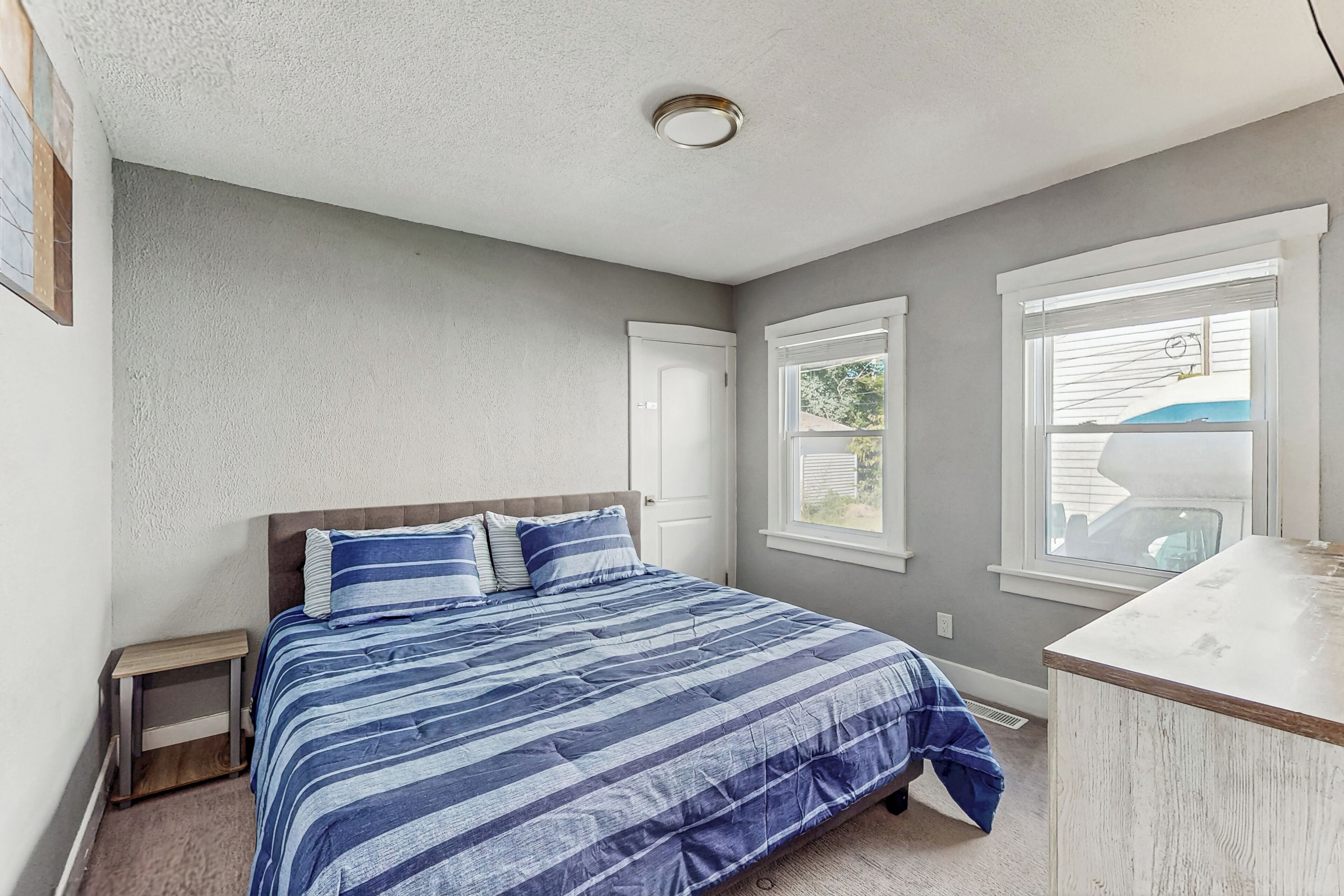 A bedroom with a bed, a nightstand, a dresser, and a window with blinds.