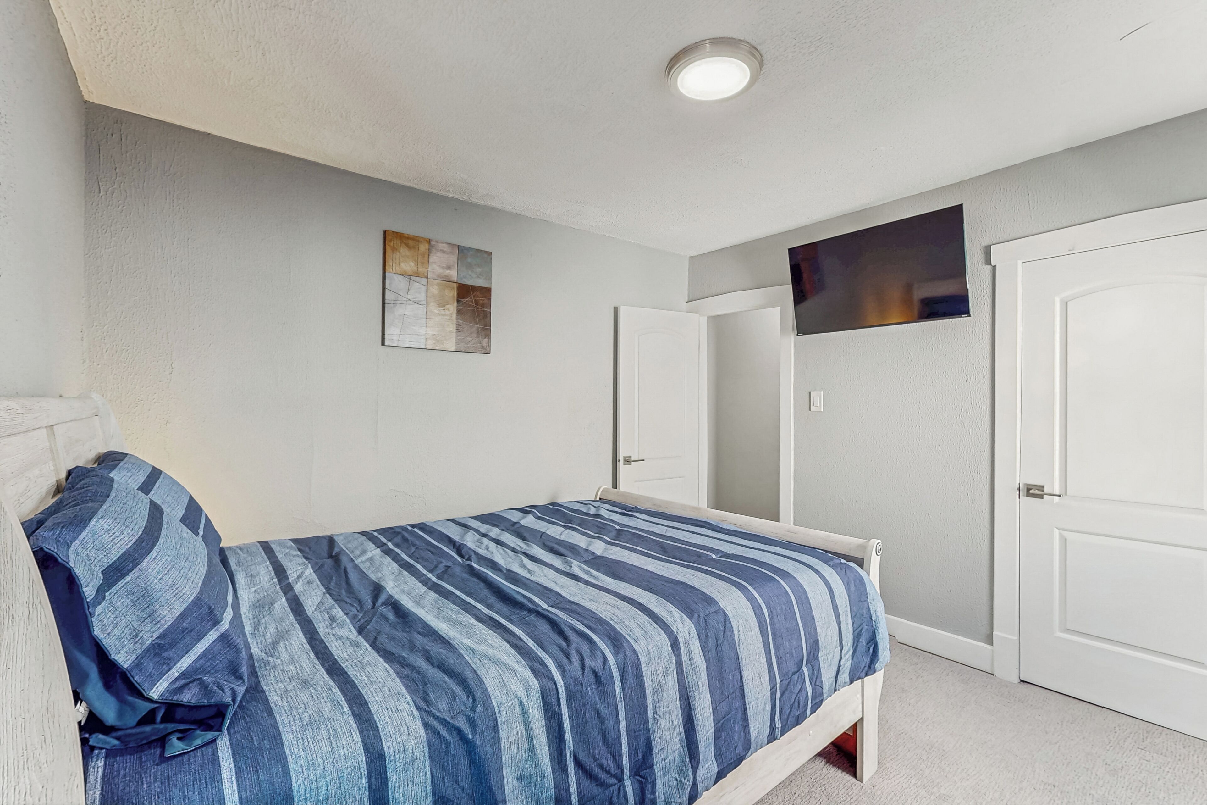 Une chambre à coucher avec un lit, une porte et un téléviseur fixé au mur.