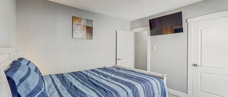 A bedroom with a bed, a door, and a wall-mounted TV.
