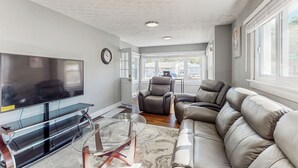 A modern living room with a flat-screen TV, leather sofas, a glass coffee table, and a large window offering a view of the outside. - Group-friendly Michigan City Home Near Beach! (Michigan City)