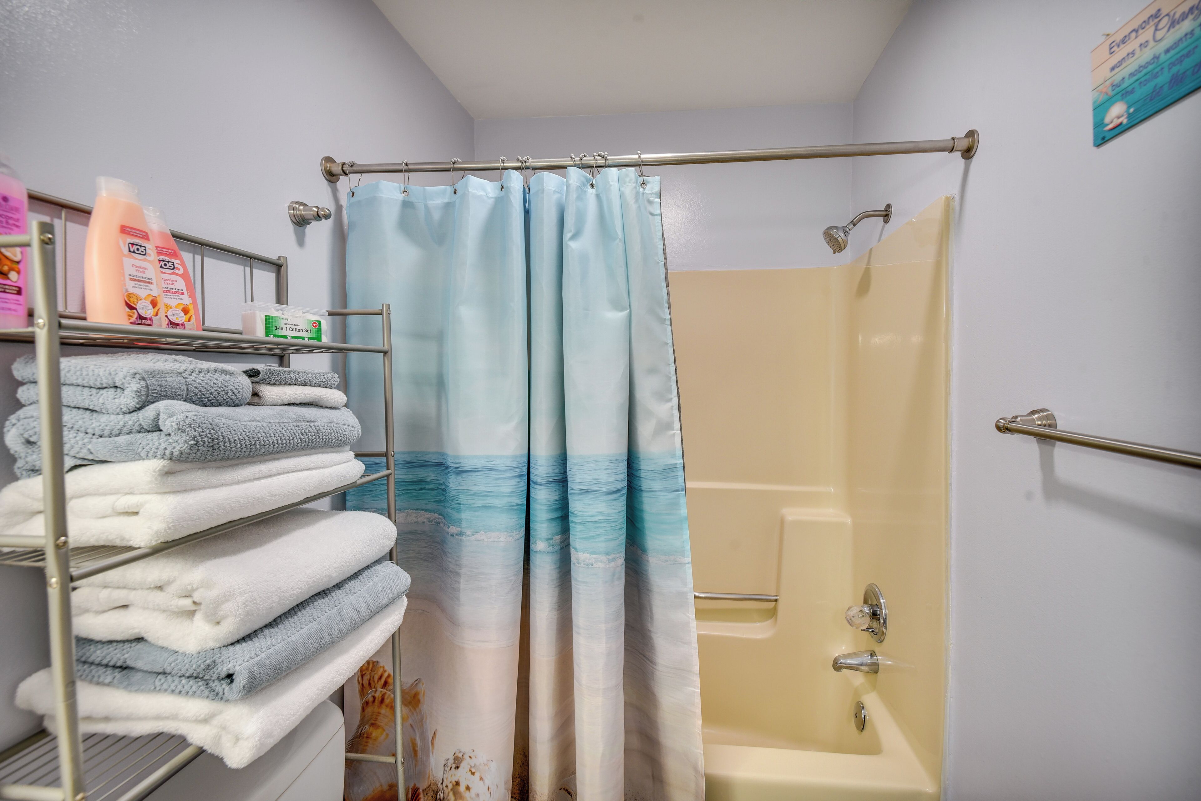A bathroom with a shower curtain, a bathtub, and a towel rack with folded towels.