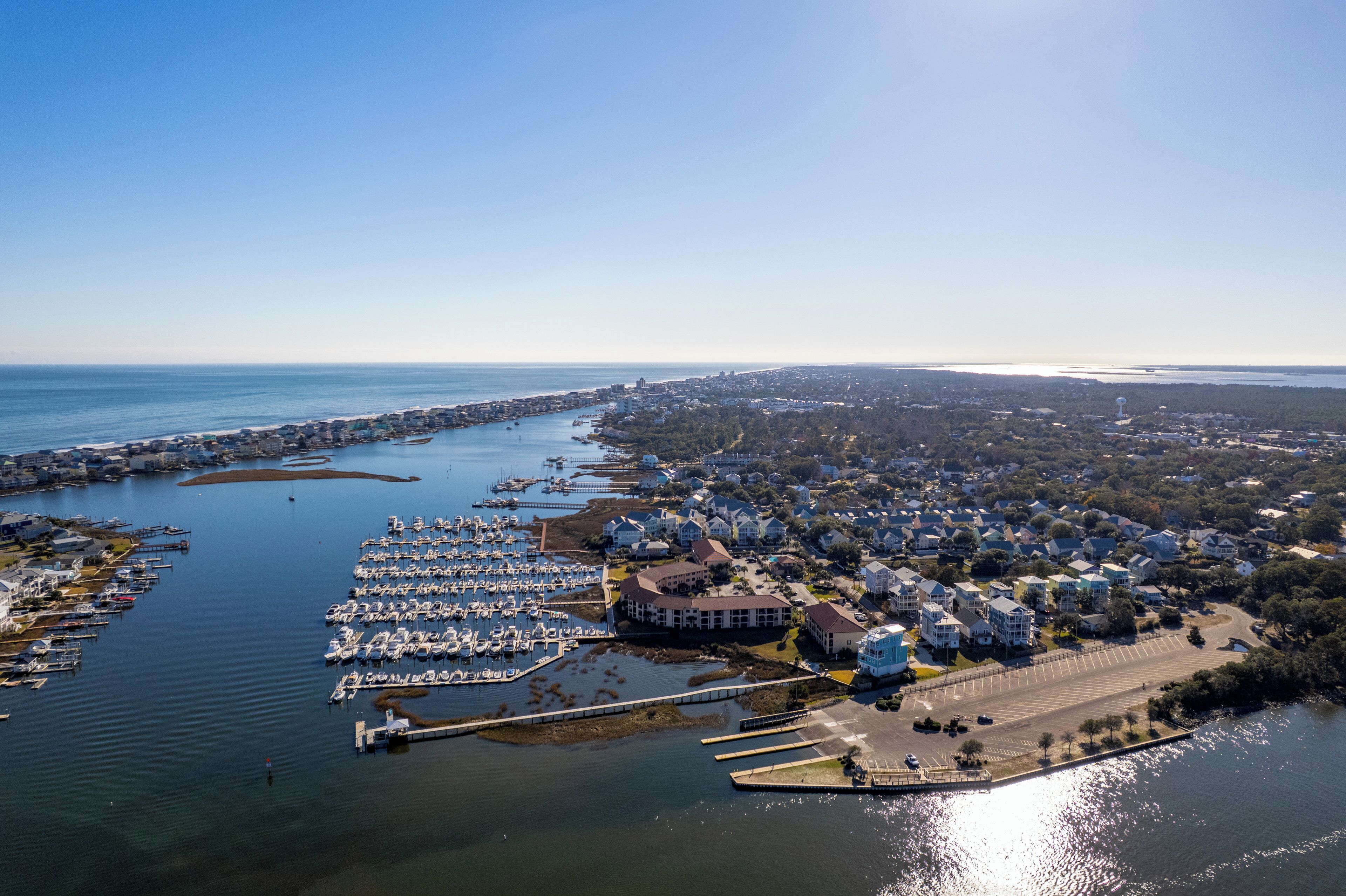 Luftaufnahme einer Küstenstadt mit einer Marina, Wohngebäuden und einem Leuchtturm.