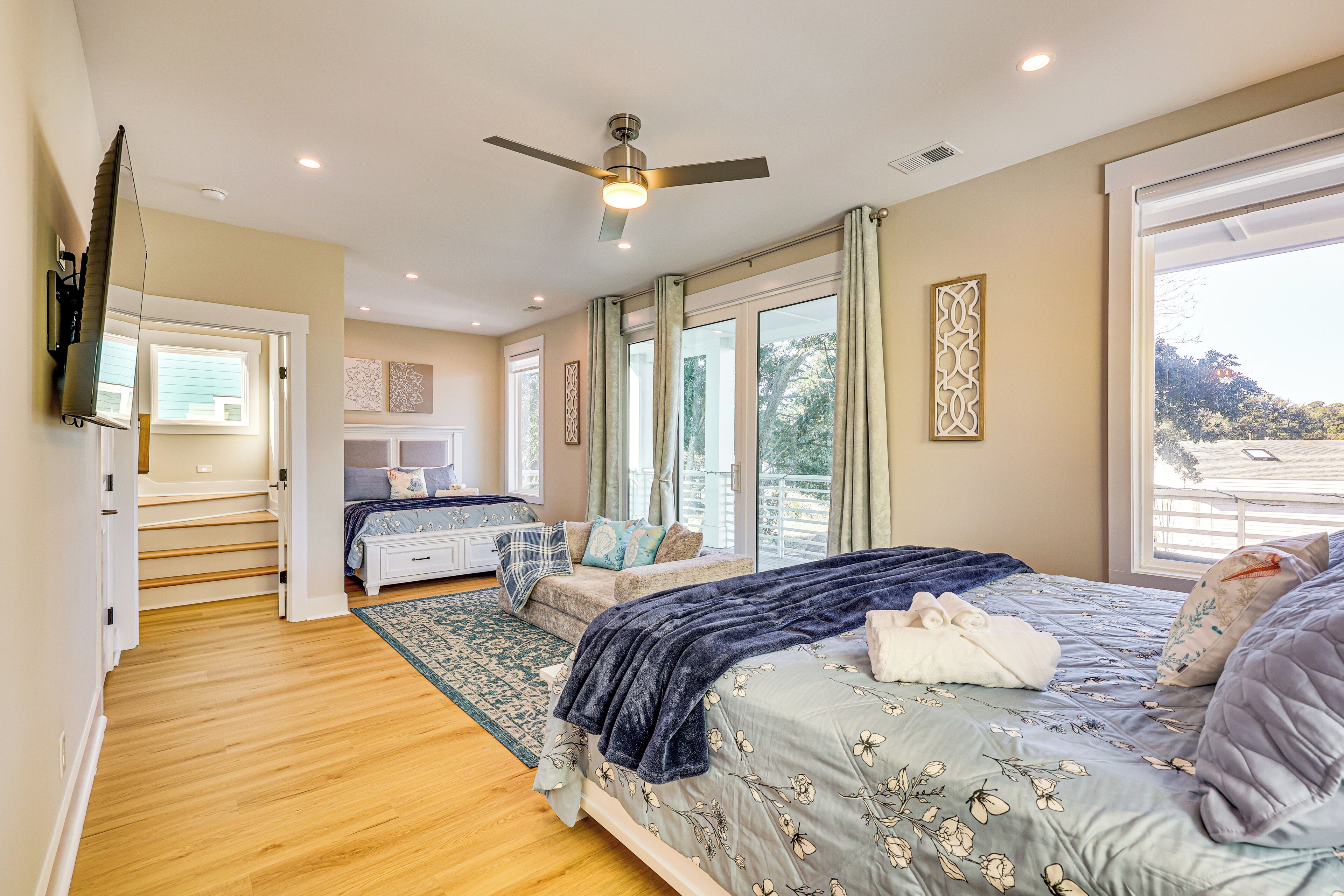 A bedroom with a large bed, a sofa, a TV, and a ceiling fan.
