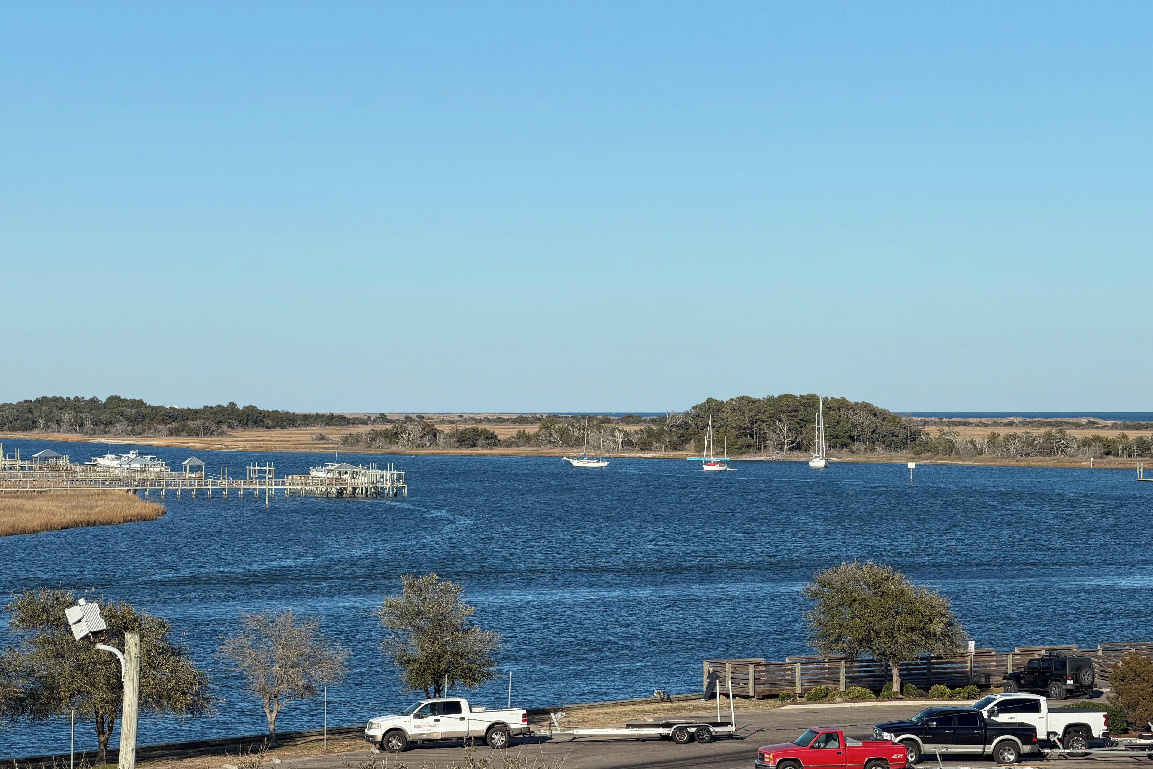A waterfront view with boats, a dock, and parked vehicles.