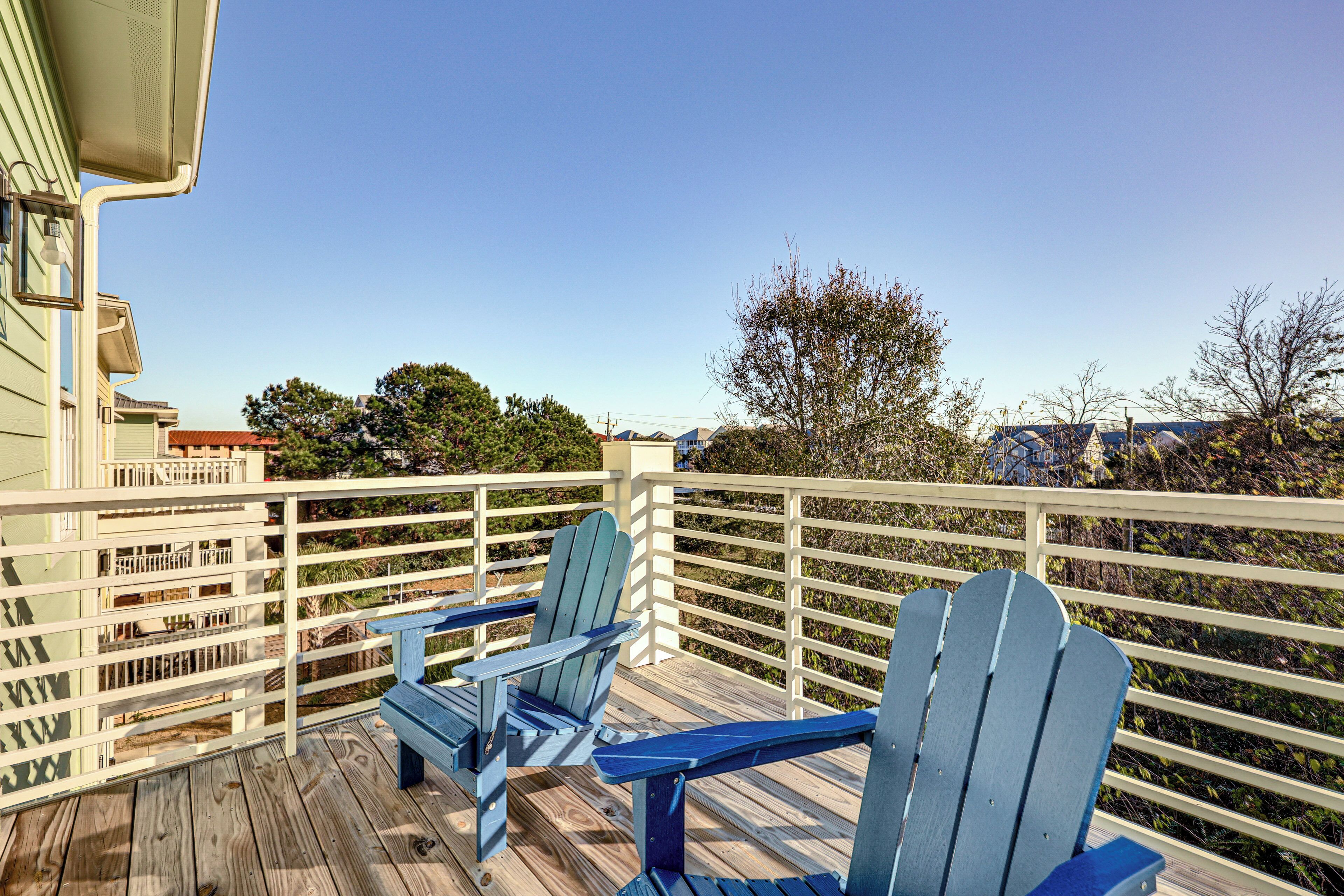 A wooden deck with two blue Adirondack chairs and a white railing.