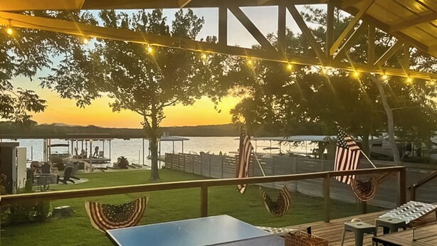 Terraza exterior con mesa de ping pong, mobiliario y vista a un cuerpo de agua al atardecer.