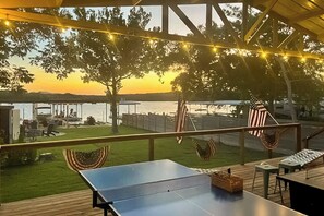 Une terrasse extérieure avec une table de ping-pong, des sièges et une vue sur un plan d’eau au coucher du soleil.