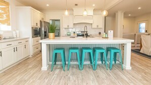 Una cocina moderna con muebles blancos, una isla central con taburetes y iluminación colgante.