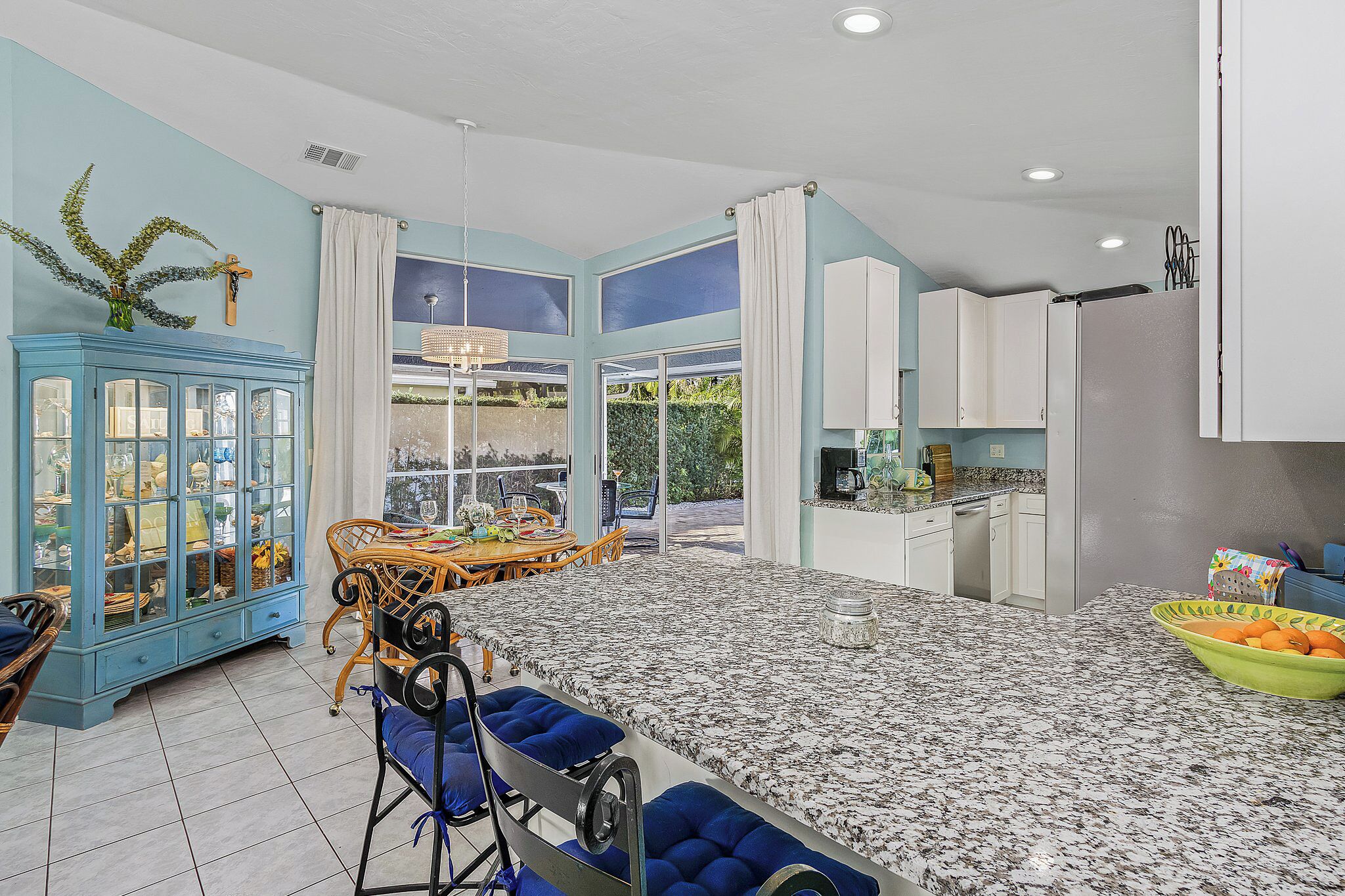 A spacious kitchen with a granite countertop, a dining area with a table and chairs, and a blue cabinet with glass doors.