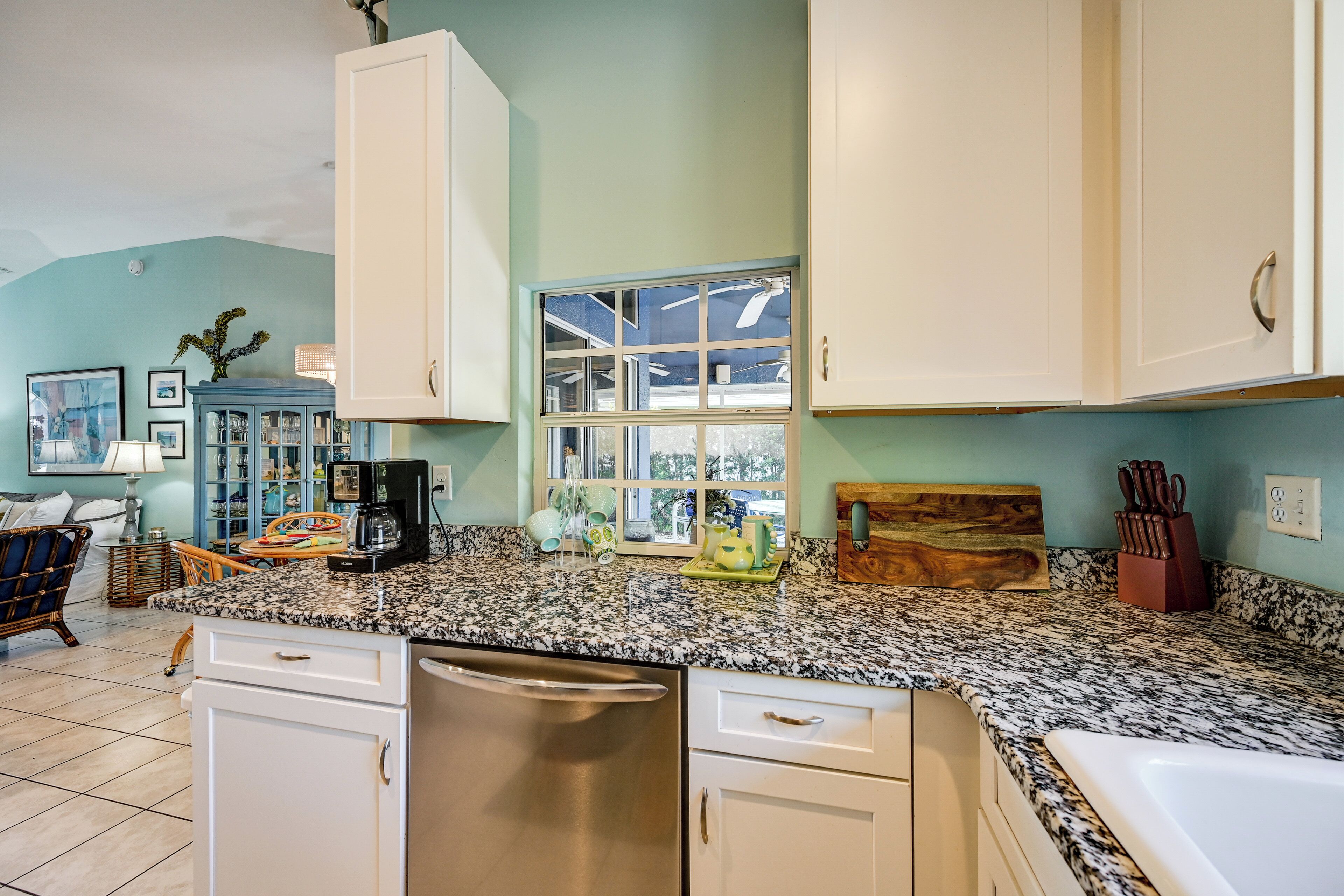 A kitchen with white cabinets, a granite countertop, and a window with a view.