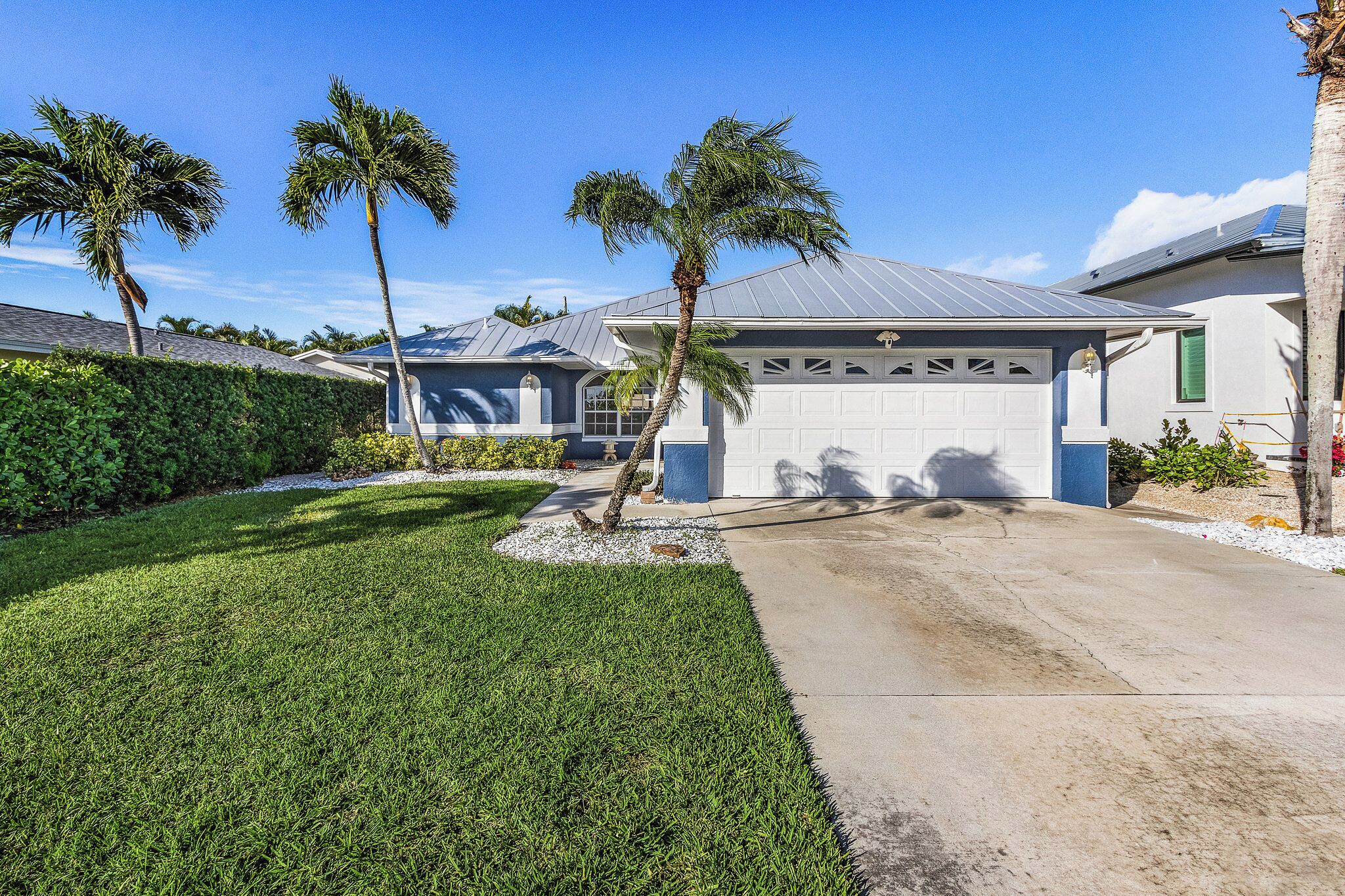 A residential house with a garage, palm trees, and a well-maintained lawn.