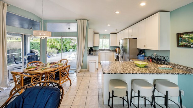 A modern kitchen with a central island, white cabinets, and a dining area with wicker chairs. - Bike to State Park: Family Getaway in Naples (Naples)