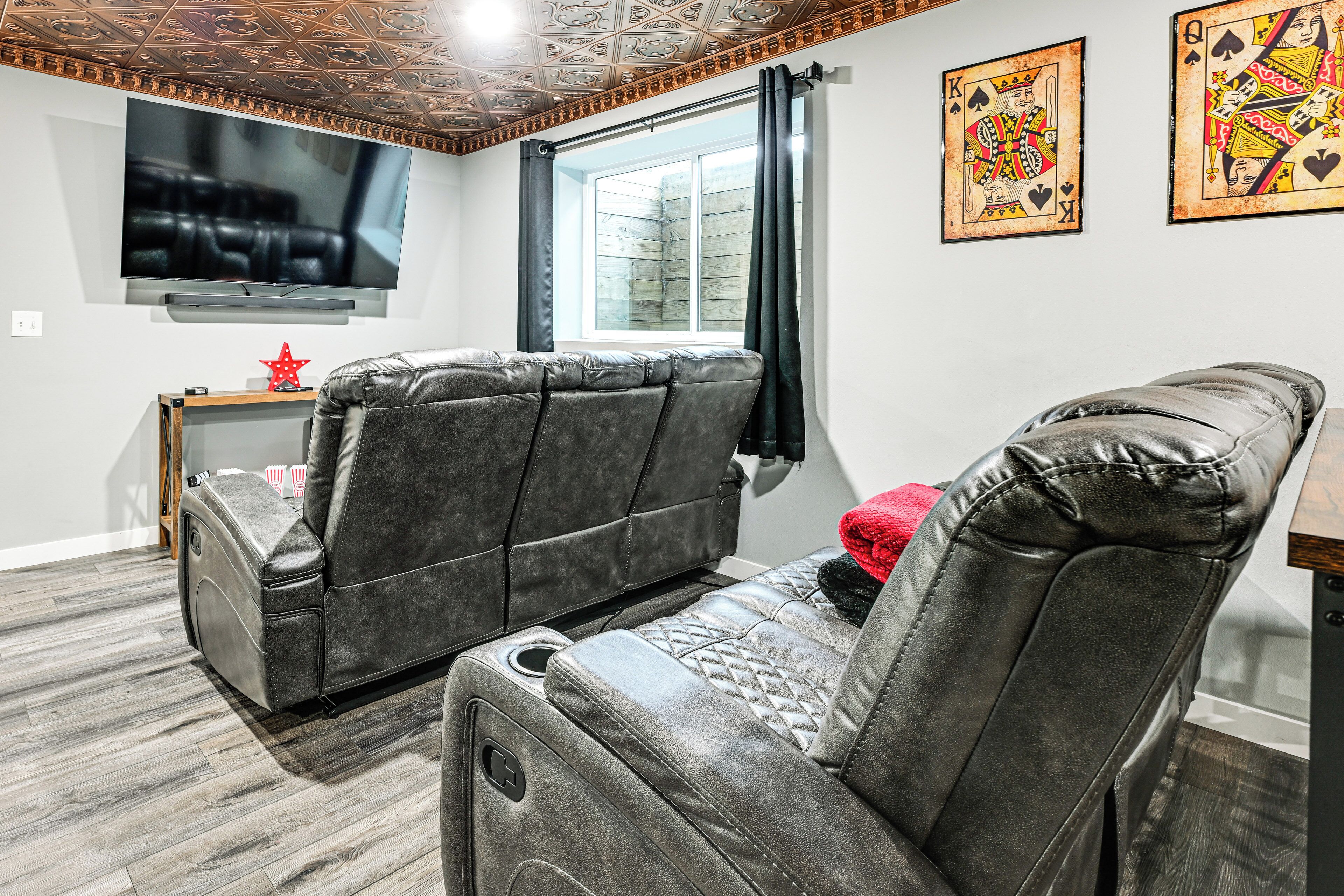 A living room with two leather recliner sofas, a flat-screen TV mounted on the wall, a window with curtains, and a framed playing card on the wall.