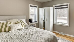Un dormitorio con cama, dos ventanas, un armario y un radiador.