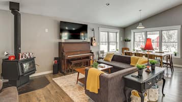 A living room with a fireplace, a piano, a sofa, and a dining area with a red lamp.