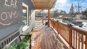 Una terraza cubierta de madera con suelo nevado, baranda de madera y un vehículo estacionado afuera.