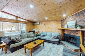 A cozy living room with a wooden ceiling, large windows, a fireplace, and a sectional sofa. - Spacious Lakefront Home w/ Private Hot Tub (White Haven)