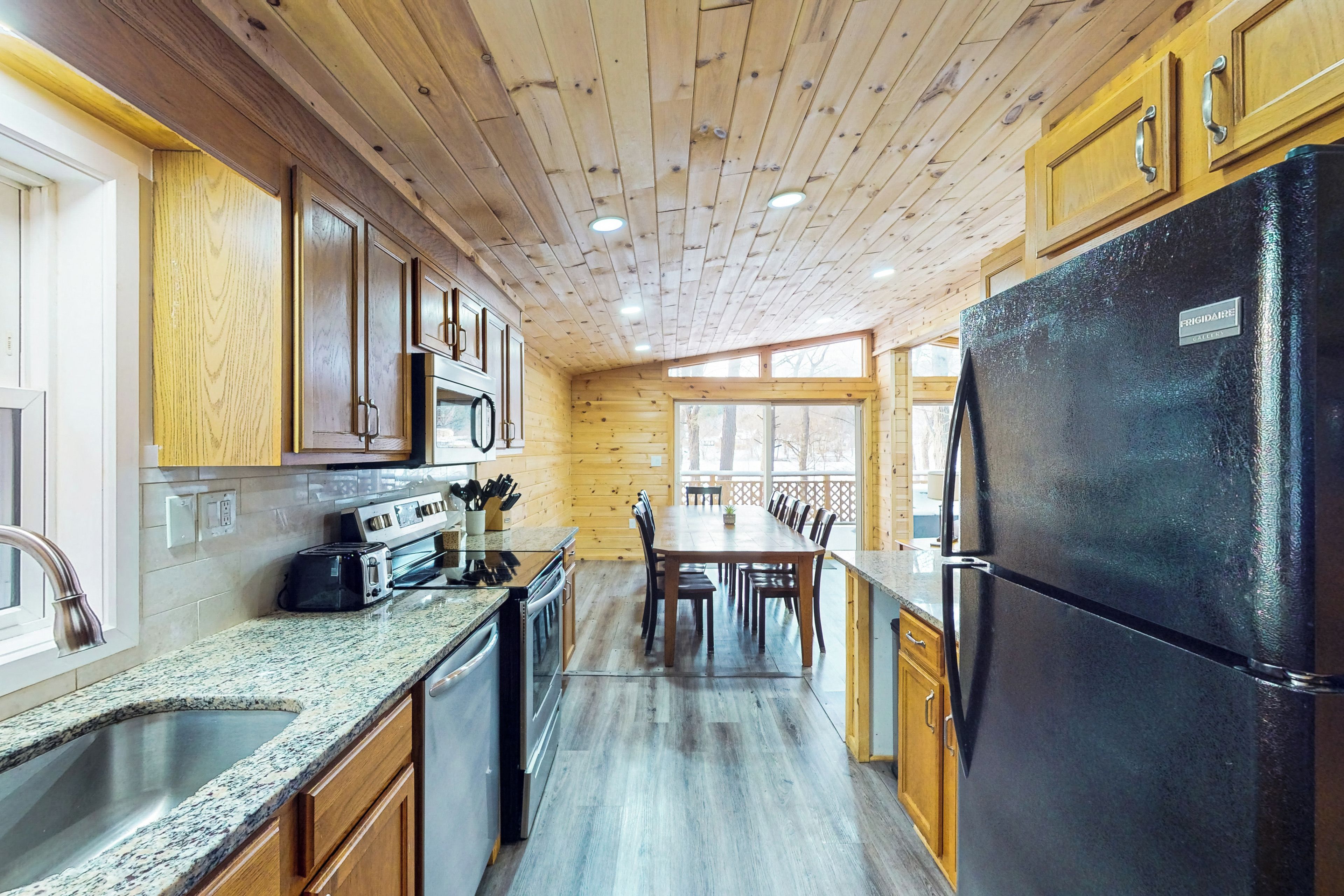 A kitchen with wooden cabinets, a black refrigerator, granite countertops, and a dining area with chairs and a table.
