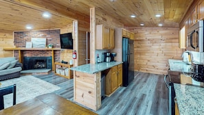 A cozy cabin-style kitchen with wooden walls, a brick fireplace, and modern appliances. - Spacious Lakefront Home w/ Private Hot Tub (White Haven)