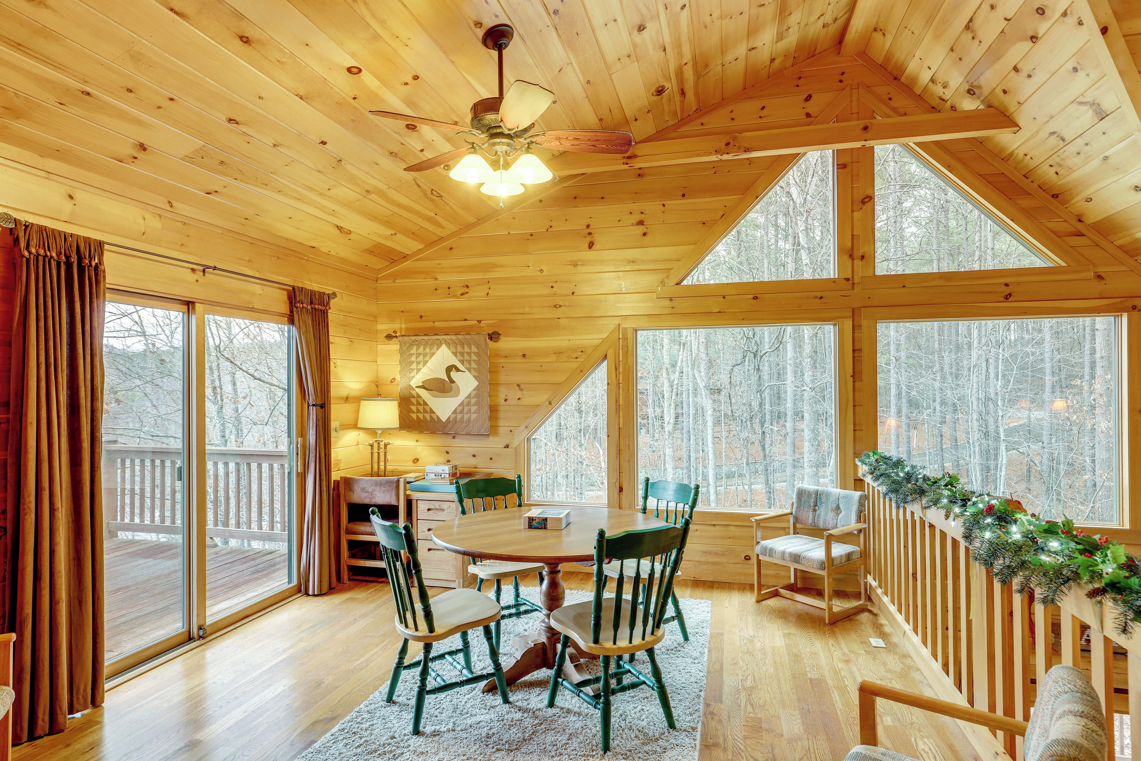 A wooden cabin interior with a dining area, large windows, and a deck.